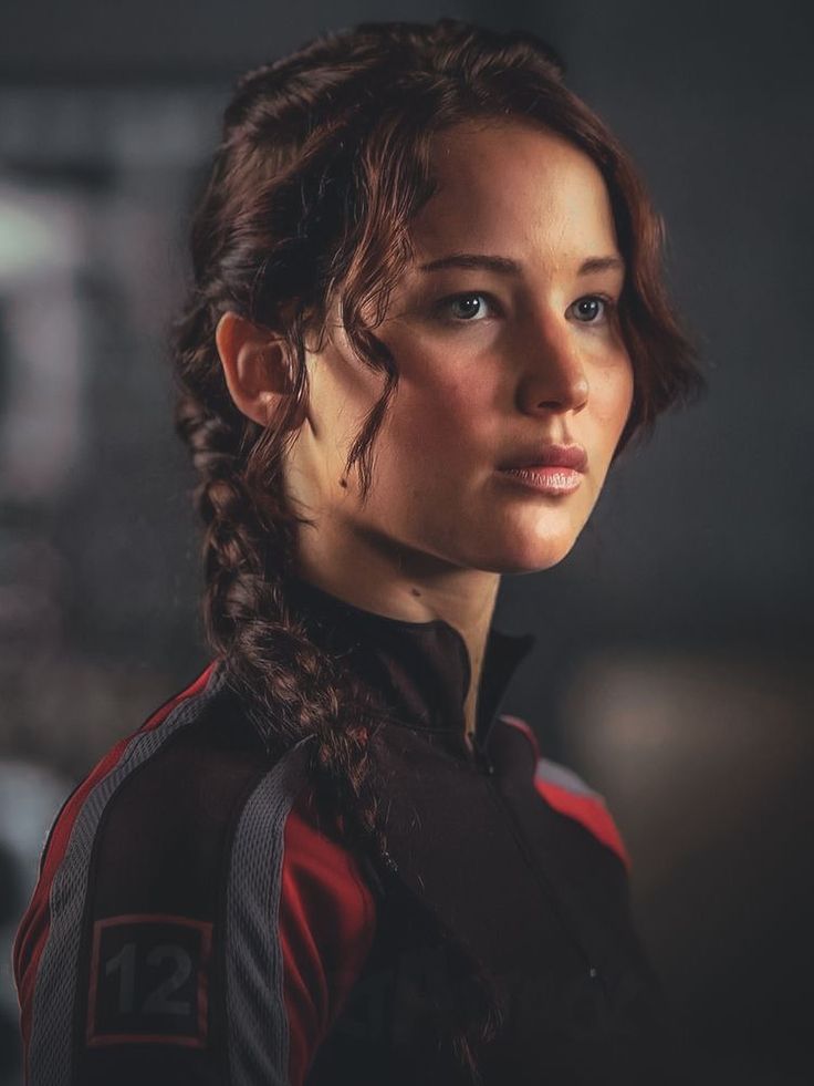 a woman with braids on her hair looks into the distance while standing in front of a dark background