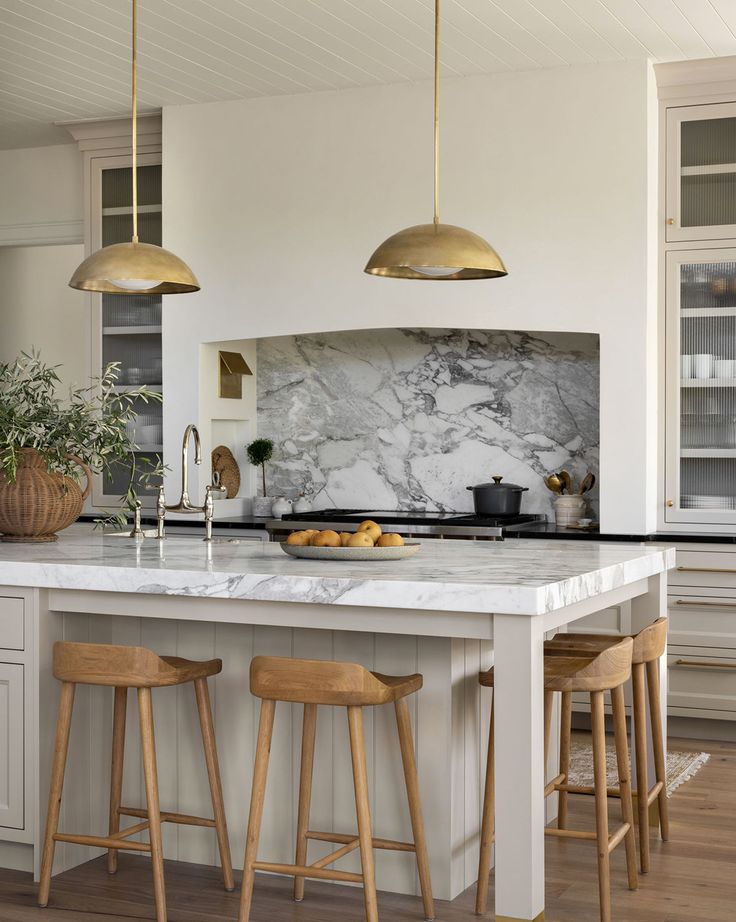 a kitchen with marble counter tops and gold pendant lights hanging over the island, along with wooden bar stools