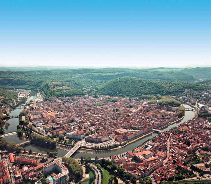 an aerial view of a river running through a city with lots of buildings and green hills in the background