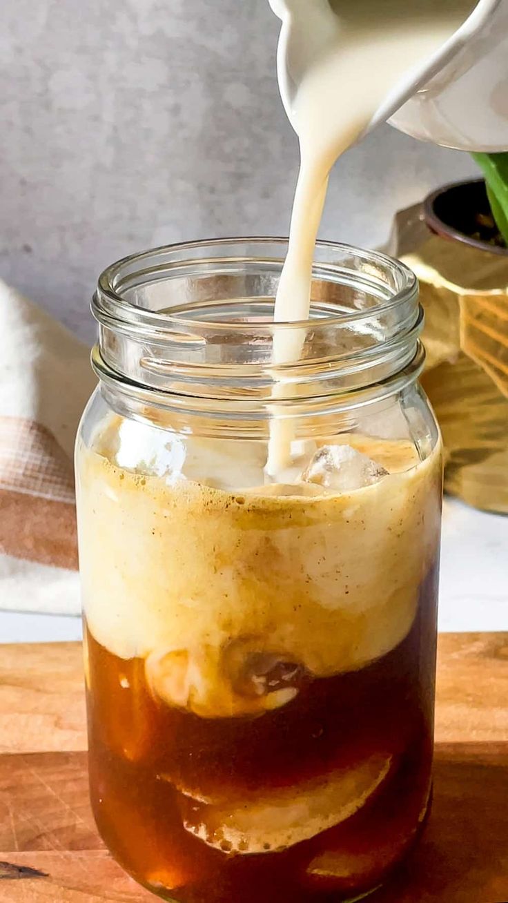 a glass jar filled with liquid and ice on top of a wooden cutting board next to a potted plant