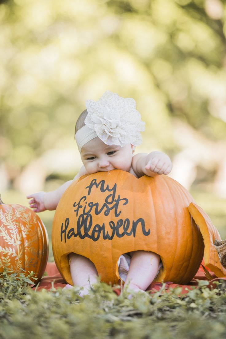 a baby sitting on top of a pumpkin with the words my first halloween written on it