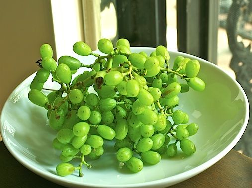 green grapes are on a white plate in front of a window sill with an open glass door