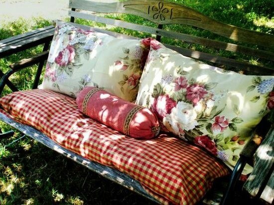 a wooden bench with pillows on it in the grass next to some flowers and trees