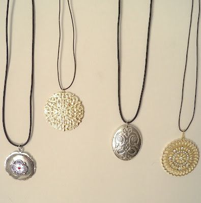 four different necklaces are hanging on a white wall, one is gold and the other is silver