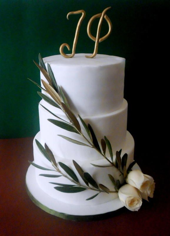 a three tiered white wedding cake with greenery and gold letters on top, sitting on a wooden table