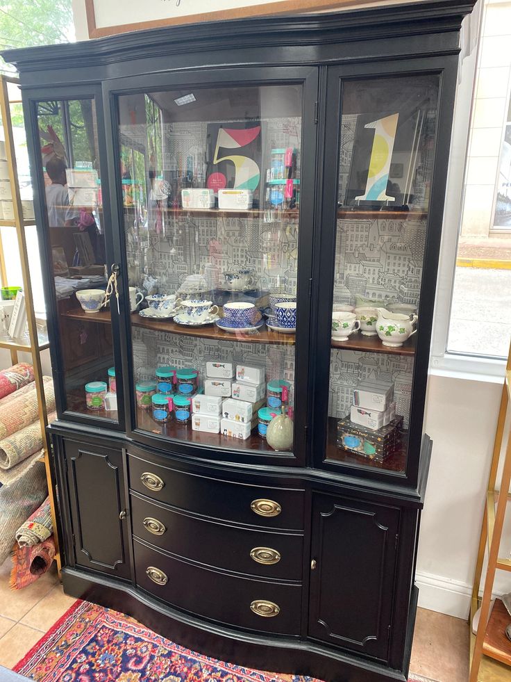 a black china cabinet with glass doors and drawers on the bottom, in front of a rug