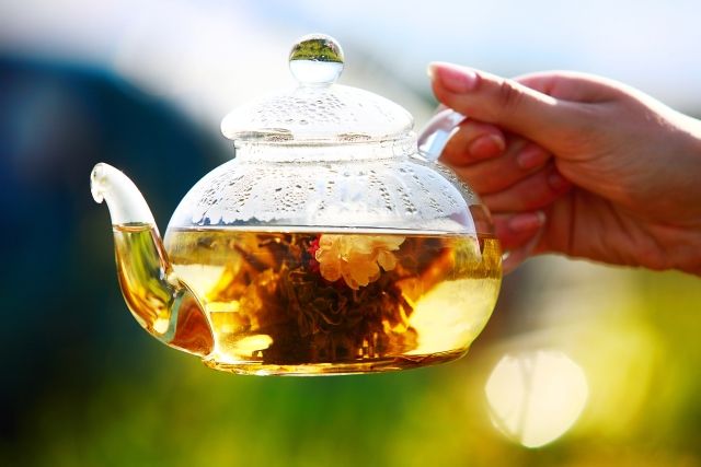 a person holding a glass tea pot filled with flowers