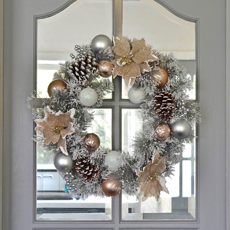 a christmas wreath with silver and gold ornaments hanging on the front door, next to a window