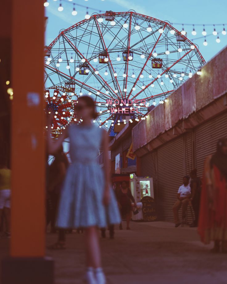 a woman in a blue dress standing next to a ferris wheel