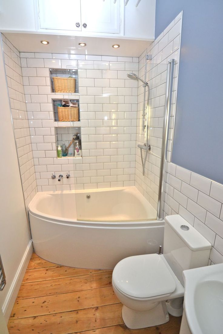 a white toilet sitting next to a bath tub in a bathroom on top of a hard wood floor