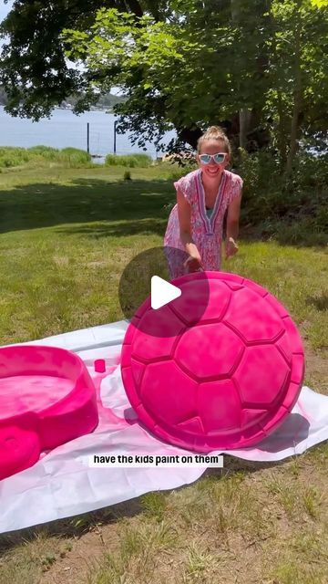 a woman standing next to a giant pink ball on top of a blanket in the grass