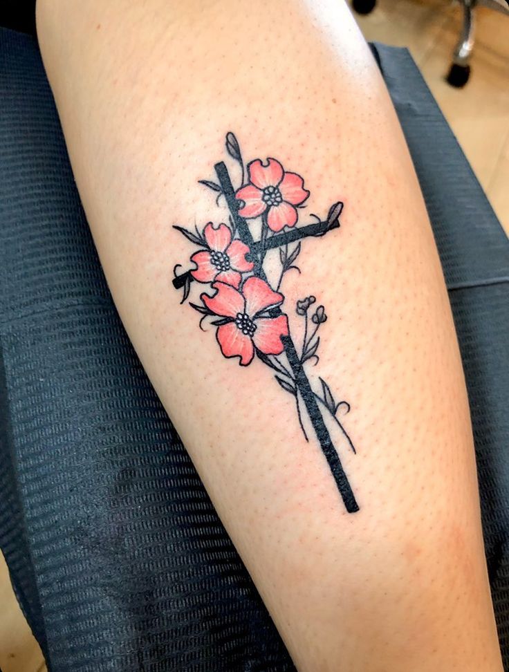 a woman's arm with a cross and flowers tattoo on the left side of her leg