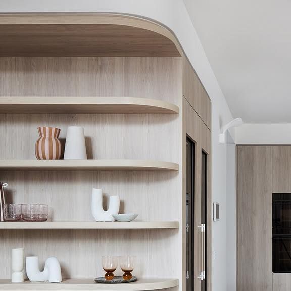 the shelves in the kitchen are made of wood and have white vases on them