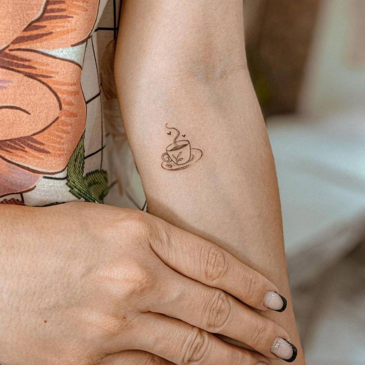 a woman's arm with a coffee cup tattoo on the left side of her arm