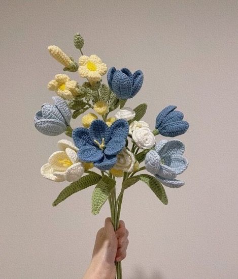 a hand holding a crocheted bouquet of flowers in front of a white wall