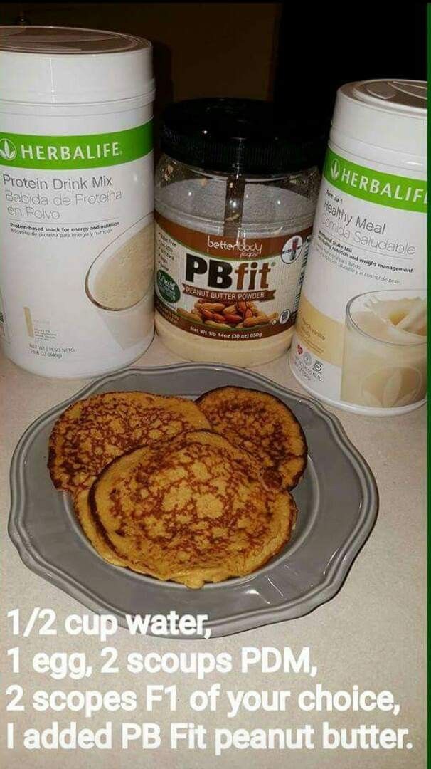 two pancakes on a plate next to some peanut butter and protein drink mix in the background