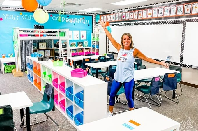 a woman is standing in the middle of a classroom with desks, chairs and bookshelves