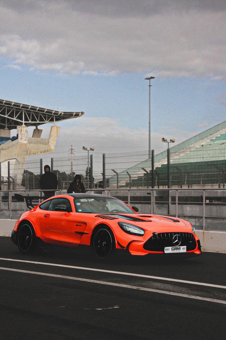 an orange sports car is driving down the road in front of a large stadium building