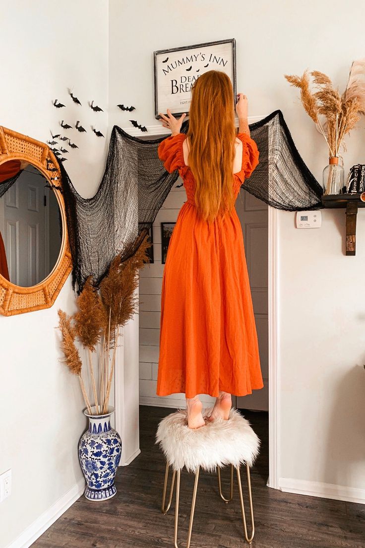 a woman in an orange dress is standing by a halloween decoration and looking at herself