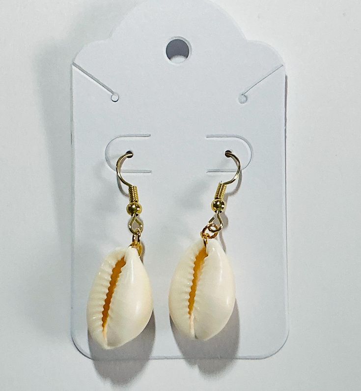 A cowrie shell with either silver or gold earring hook. Gold Teardrop Earrings For The Beach, Cowrie Shell Dangle Earrings As Gift, Teardrop Hoop Earrings With Ear Wire For Beach, Cowrie Shell Dangle Jewelry Gift, Cowrie Shell Dangle Jewelry For Gifts, Shell Earrings With Ear Wire For Vacation, Beach Teardrop Jewelry With Ear Wire, Teardrop Ear Wire Jewelry For Beach, White Shell-shaped Cowrie Shell Earrings