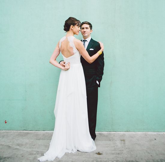 a man and woman standing next to each other in front of a green wall holding an umbrella