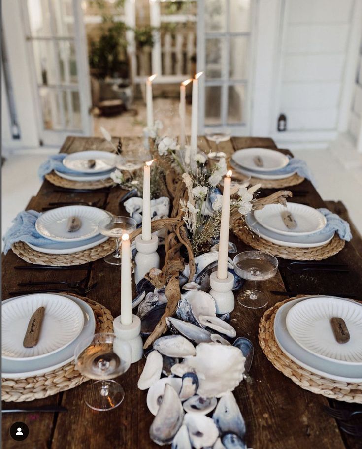 the table is set with plates, candles and seashells for an elegant dinner