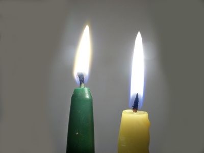 two candles with one lit and the other turned on, sitting in front of a white wall