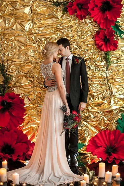 a man and woman standing next to each other in front of a gold wall with red flowers