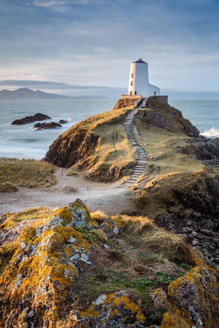 a light house on top of a rocky hill next to the ocean with moss growing around it