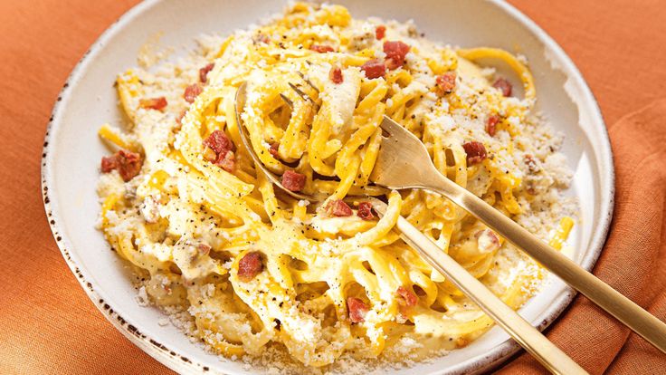 a white plate topped with pasta covered in cheese and bacon next to a wooden spoon