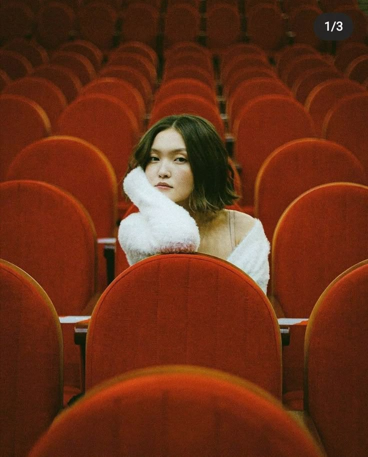 a woman sitting in an empty auditorium with her hands on her face and looking off to the side