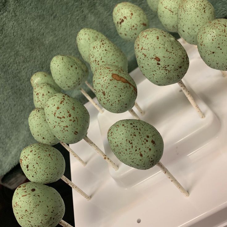 there are many green cake pops with brown speckles on them sitting on a white tray