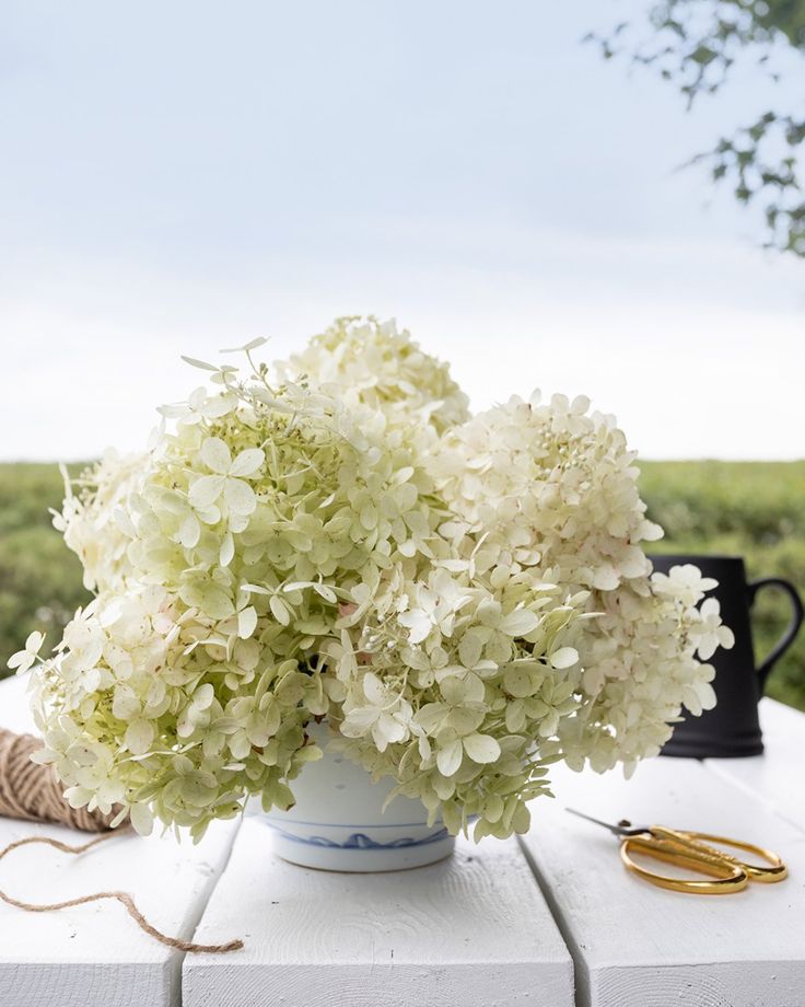 a white vase filled with flowers sitting on top of a table next to scissors and yarn