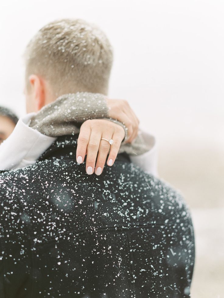 a man and woman embracing each other in the snow with their hands on his back