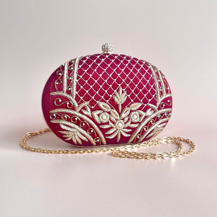 A timeless and classic piece, handcrafted with detailed embroidery and pearl beads. The maroon tones and gold threaded embroidery adds a luxurious feel to the bag and brings the statement factor to your look. With one main compartment and a magnetic fastening, this grande clutch is completed with a chain strap which can be worn as a shoulder bag or tucked in for a clutch style. Elegant Embroidered Fabric With Pearl Embroidery For Reception, Elegant Pearl Embroidered Fabric For Reception, Elegant Hand-embellished Embroidered Fabric For Festive, Elegant Formal Embroidered Fabric With Intricate Embroidery, Festive Embroidered Evening Bags, Elegant Hand Embellished Embroidered Fabric For Festive, Elegant Intricate Embroidery Fabric For Evening, Elegant Hand Embellished Embroidered Fabric For Festive Season, Festive Evening Embroidered Bags