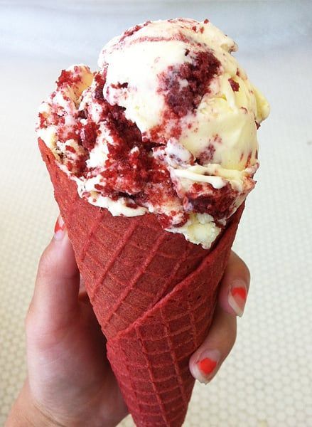 a hand holding an ice cream cone with red and white toppings