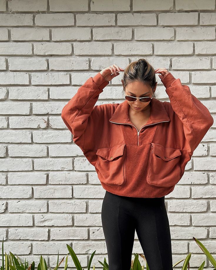 a woman standing in front of a brick wall with her hands on her head and wearing black leggings