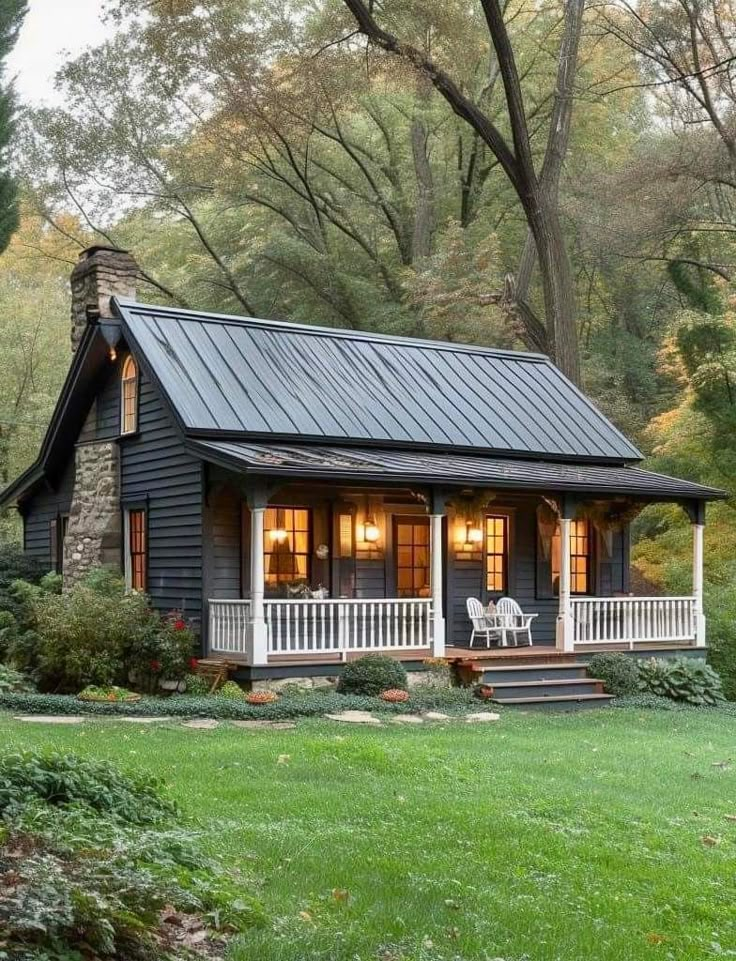 a small black house with a porch and covered front porch in the middle of trees