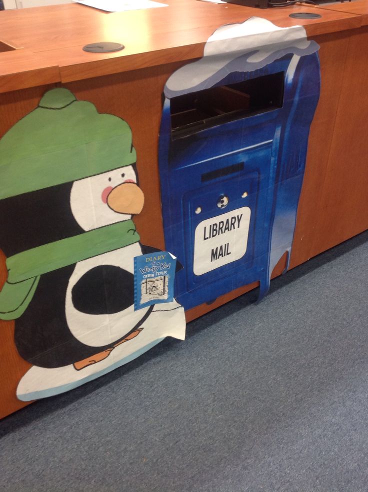 a library mailbox with a penguin painted on it's side next to a wooden desk