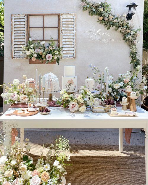 a table with flowers and candles on it in front of a white wall that has shutters