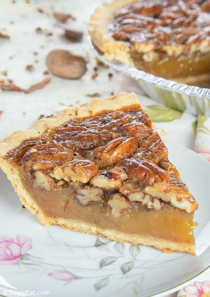 a slice of pecan pie on a plate with another pie in the back ground