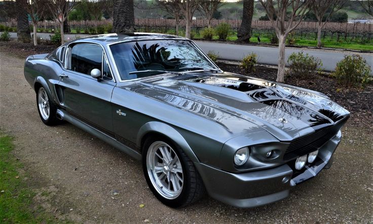 an old mustang muscle car parked on the side of a road in front of some trees