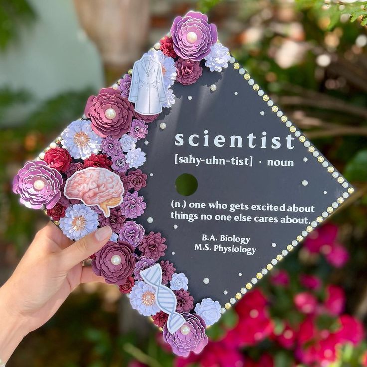 a person holding up a graduation cap with flowers on it that says, scientist baby - un - first