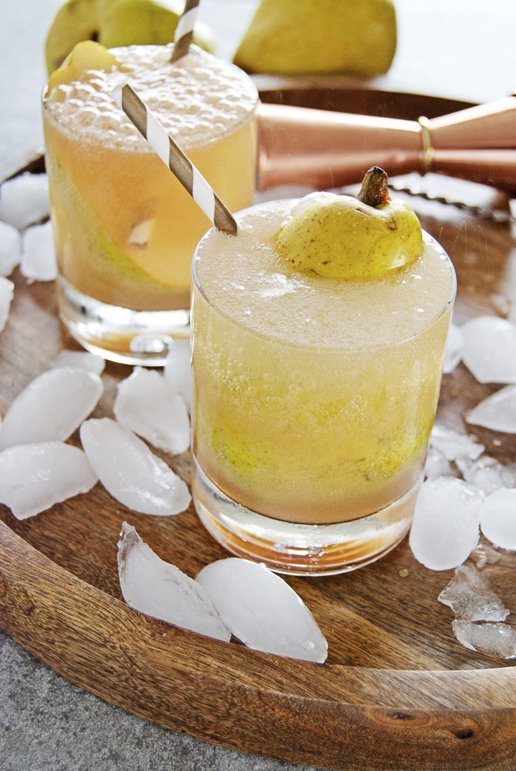 two glasses filled with lemonade and an apple sitting on top of ice cubes