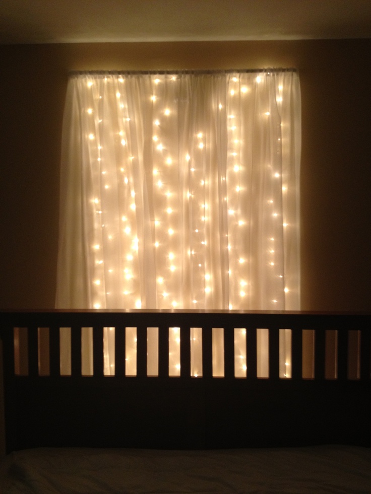 the lights are shining on the curtain behind the bed in front of the window,