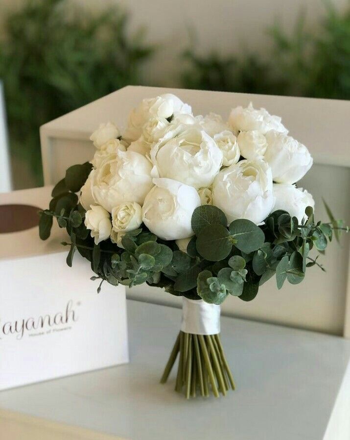 a bouquet of white roses and greenery sits on a table next to a card