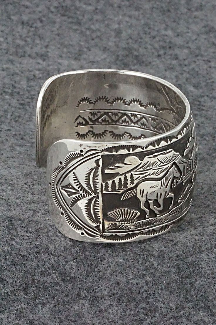 This sterling silver bracelet featuring horses grazing in a Southwestern landscape was made by Navajo silversmith Jeremy Delgarito. The back is signed J Delgarito and stamped sterling.Size: 5 3/8" (will fit up to a 6 3/4" wrist)Gap: 1 3/8"Width: 1 1/4"Free shipping on all orders! We ship with USPS and always include tracking. All orders ship within a day of payment.Returns are accepted up to 30 days after you receive your order. Just send us a message. Our shop offers cash back or store credit. Southwestern Engraved Sterling Silver Bracelet Gift, Handmade Western Silver Cuff Bracelet, Engraved Sterling Silver Bracelet Gift, Southwestern Sterling Silver Bracelet Stamped 925 As Gift, Western Sterling Silver Cuff Bracelet Gift, Handmade Western Sterling Silver Bracelet For Gift, Adjustable Western Sterling Silver Bracelet For Gift, Western Sterling Silver Bracelets With Concho, Western Sterling Silver Concho Bracelets