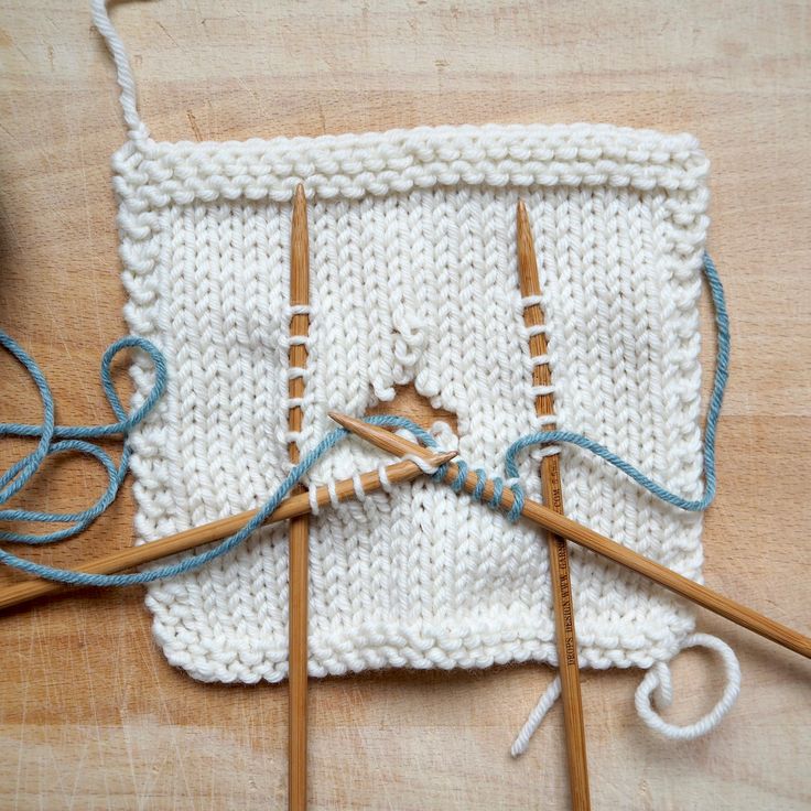 two knitting needles are hooked up to yarn on a wooden surface, next to an object that appears to be crocheted