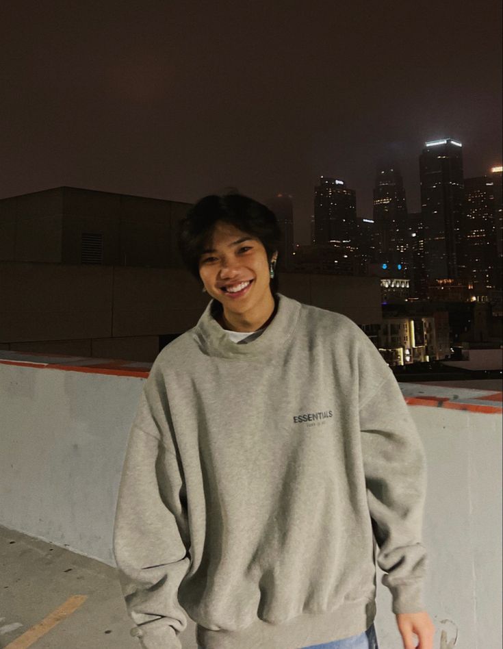 a young man standing on top of a roof next to a tall building at night