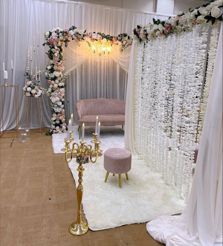 a decorated stage with candles and flowers on the wall, surrounded by white drapes